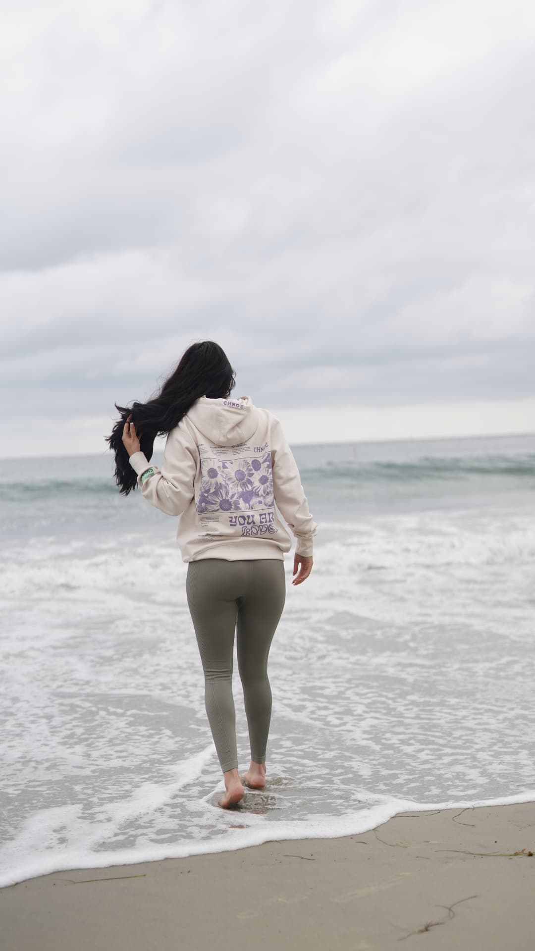 Woman walking on the shoreline in a YOU ARE LOVED hoodie